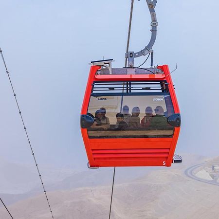Tolip Resort El Galala Majestic Ain Suchna Exterior foto The photo shows a red gondola lift suspended in the air, traveling along cables. Inside the gondola, a group of people can be seen. The background features a hazy landscape, possibly mountains or hills, indicating an elevated area. The scene conveys 