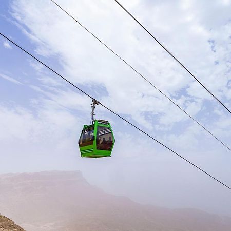 Tolip Resort El Galala Majestic Ain Suchna Exterior foto The photo shows a green cable car suspended in the air, traveling along overhead cables. The backdrop features a hazy landscape, likely mountainous or elevated terrain, with a cloudy sky. The scene suggests a scenic transportation method, possibly us