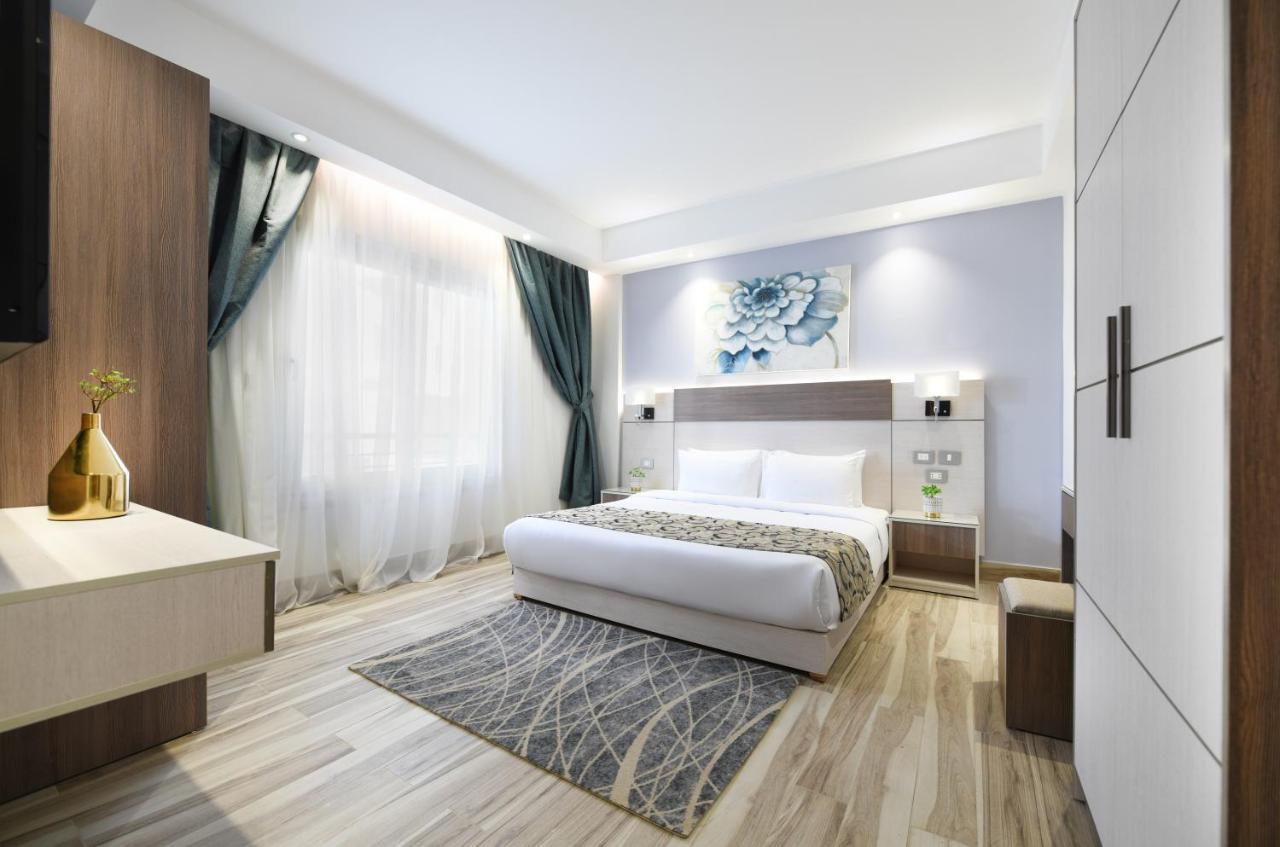 Tolip Resort El Galala Majestic Ain Suchna Exterior foto The photo shows a modern bedroom with a clean and stylish design. It features a large bed with white bedding positioned against a wall. Above the bed, there is a decorative artwork, possibly a floral design. The room has large windows with sheer curt