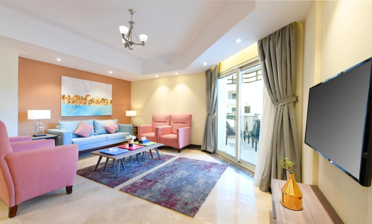 Tolip Resort El Galala Majestic Ain Suchna Zimmer foto The photo shows a modern living room that features a cozy and stylish design. There is a light blue sofa adorned with pastel pink cushions, accompanied by two pink armchairs. A coffee table sits in front, placed on a colorful area rug that adds warmt