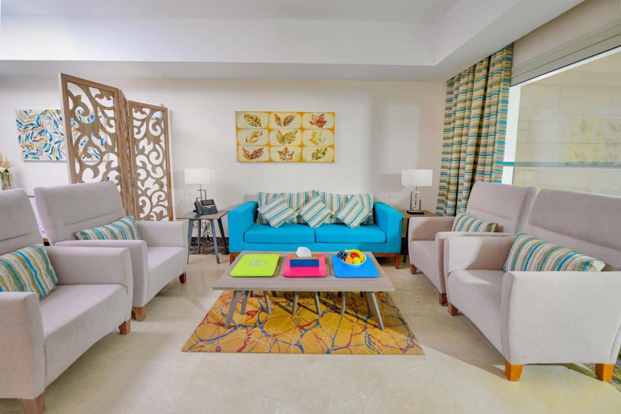 Tolip Resort El Galala Majestic Ain Suchna Exterior foto The photo shows a stylish and colorful living room. It features a bright blue sofa with patterned cushions, complemented by two light gray armchairs. In front of the sofa, there's a wooden coffee table with vibrant trays in pink, green, and yellow. A