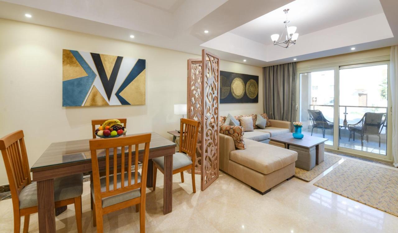 Tolip Resort El Galala Majestic Ain Suchna Exterior foto The photo shows a modern and stylish interior of a living space. It features a seating area with a plush sofa and decorative cushions, complemented by a wooden coffee table. There is a dining table with wooden chairs nearby. 

On the walls, there are