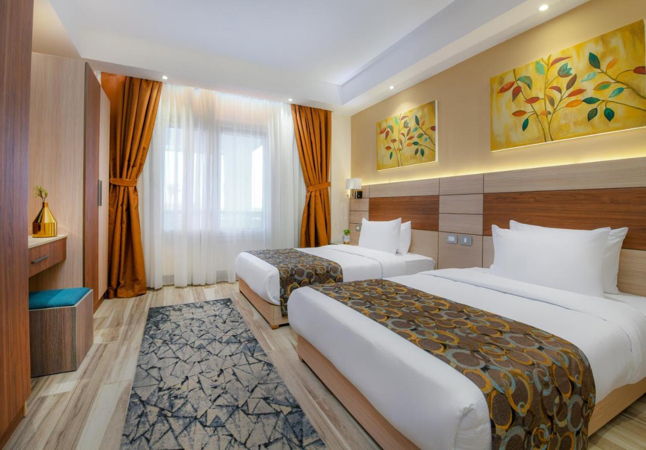 Tolip Resort El Galala Majestic Ain Suchna Exterior foto The photo shows a modern hotel room with two single beds, each covered with white linens and decorative brown bed throws. The walls are painted in warm colors, and there are two pieces of artwork featuring floral and leaf designs above the beds. The 