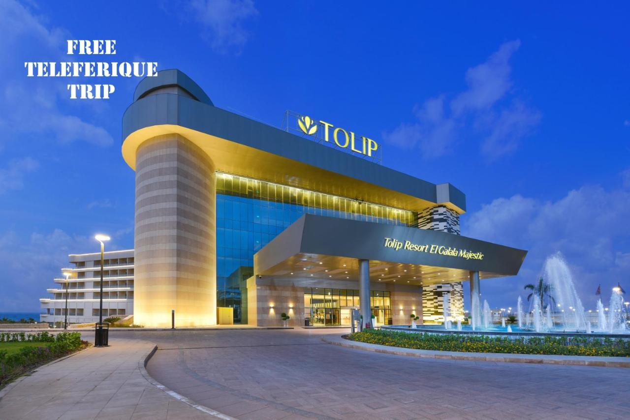 Tolip Resort El Galala Majestic Ain Suchna Exterior foto The photo shows a modern hotel building named "Tolip Resort & Spa," featuring a sleek architectural design with large glass windows. The hotel is illuminated against a twilight sky, showcasing its prominent signage. In the foreground, there is a well