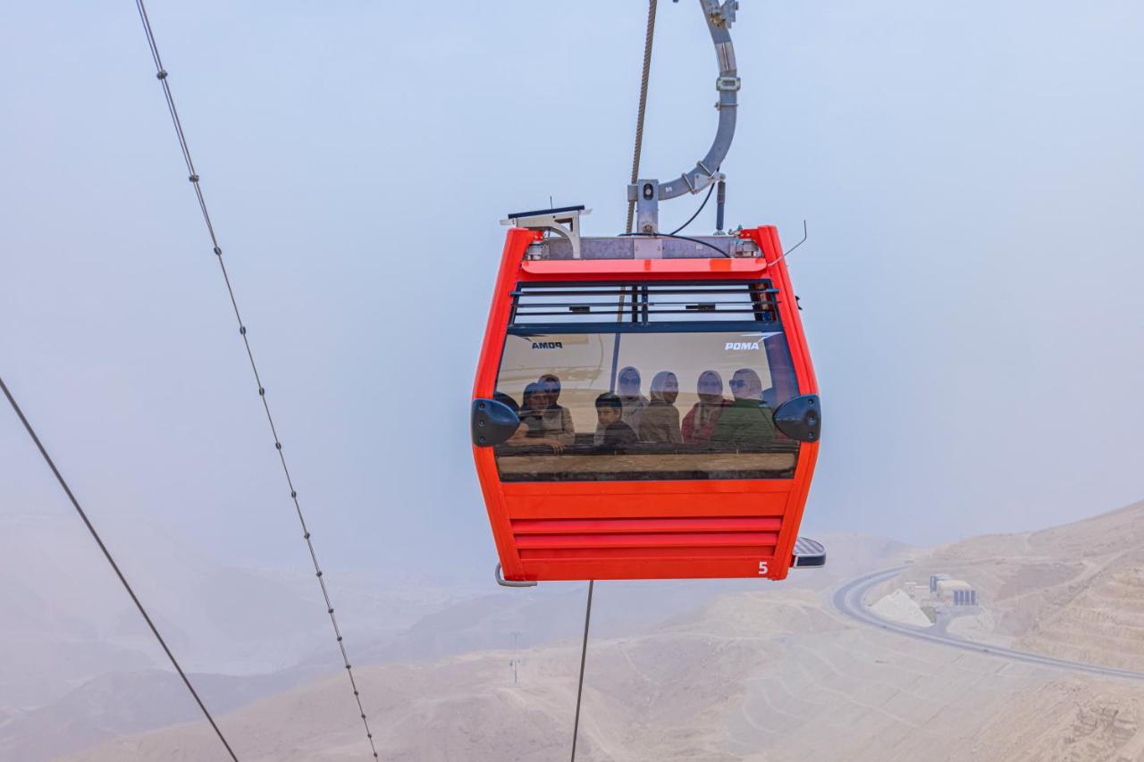 Tolip Resort El Galala Majestic Ain Suchna Exterior foto The photo shows a red gondola lift suspended in the air, traveling along cables. Inside the gondola, a group of people can be seen. The background features a hazy landscape, possibly mountains or hills, indicating an elevated area. The scene conveys 