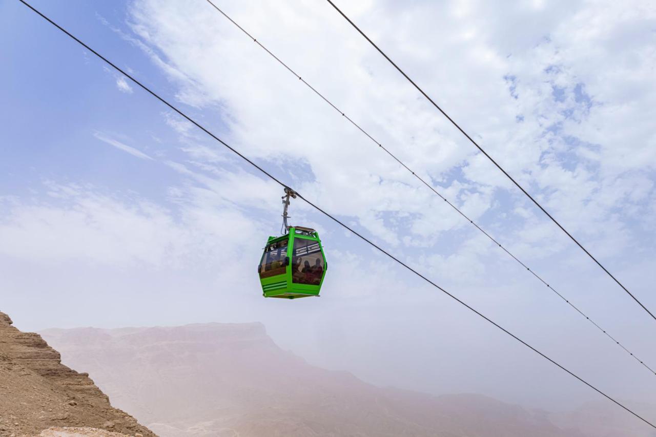 Tolip Resort El Galala Majestic Ain Suchna Exterior foto The photo shows a green cable car suspended in the air, traveling along overhead cables. The backdrop features a hazy landscape, likely mountainous or elevated terrain, with a cloudy sky. The scene suggests a scenic transportation method, possibly us