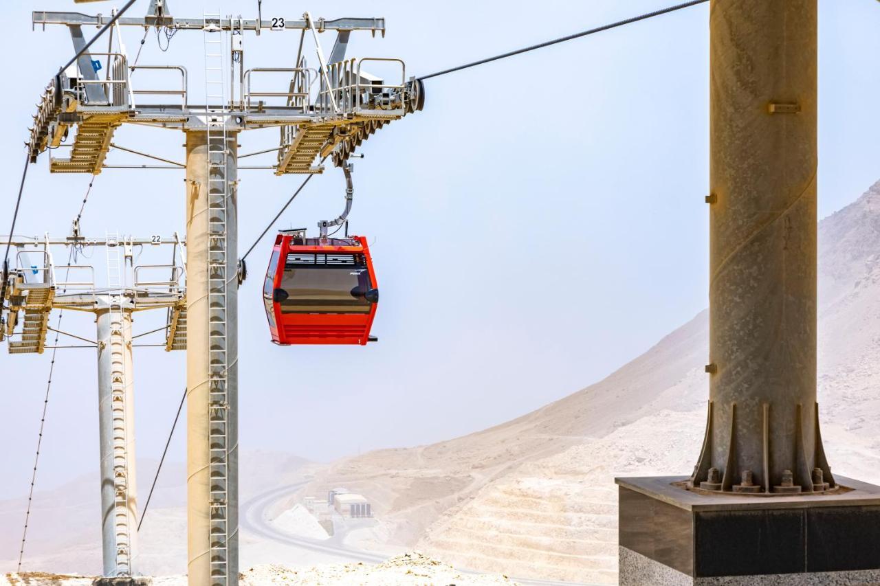 Tolip Resort El Galala Majestic Ain Suchna Exterior foto The photo shows a cable car system with a single red gondola suspended mid-air. It appears to be part of a larger cable car infrastructure, with metal pylons supporting the cables above. The background features a hazy landscape, likely characterized 