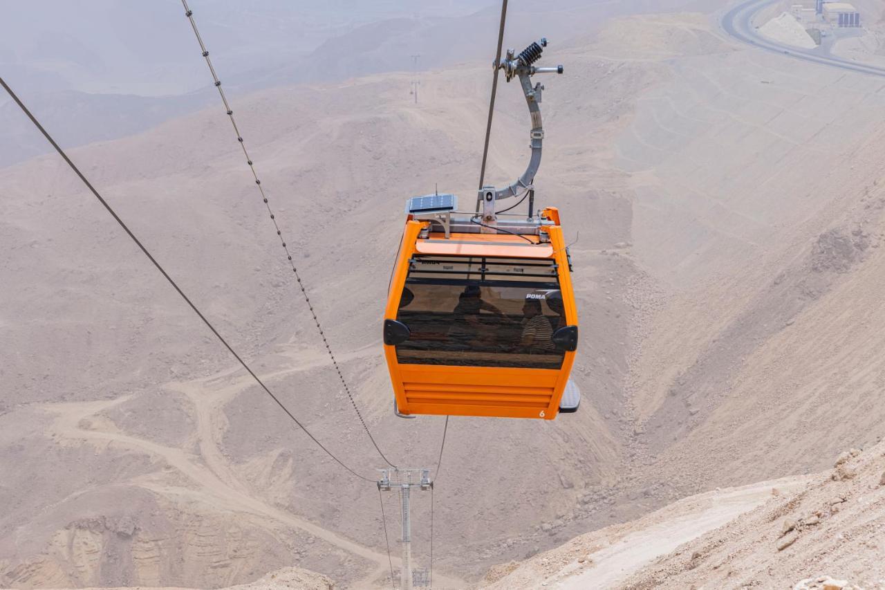 Tolip Resort El Galala Majestic Ain Suchna Exterior foto The photo shows an orange cable car suspended in the air, traveling along a set of cables. It appears to be located in a mountainous or hilly area, with rugged terrain and dry, rocky landscapes visible below. The background features slopes that seem 