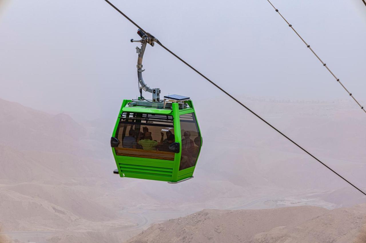 Tolip Resort El Galala Majestic Ain Suchna Exterior foto The photo shows a green cable car suspended in the air, moving along a wire. The cable car appears to be traversing a mountainous landscape, which looks rocky and arid. The surrounding environment is somewhat foggy or hazy, suggesting limited visibil