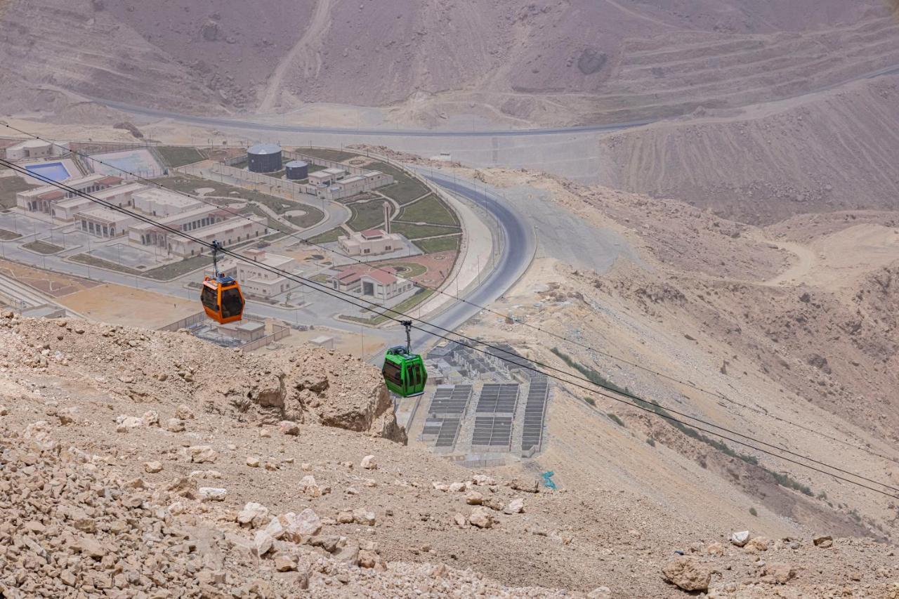 Tolip Resort El Galala Majestic Ain Suchna Exterior foto The photo shows a scenic view from a high elevation, featuring a cable car system. Two cable cars are visible, one orange and one green, traveling along cables down the mountainside. Below, there appears to be a developed area with roads and light st