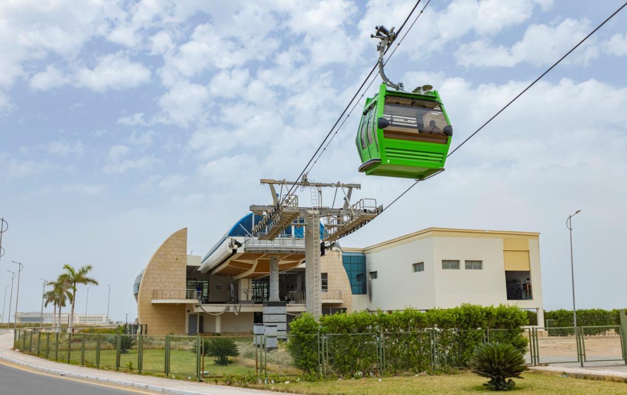 Tolip Resort El Galala Majestic Ain Suchna Exterior foto The photo shows a cable car or gondola system in operation, featuring a green-colored gondola. It is suspended from cables and moving towards a station, which appears to be a modern building with a unique architectural design. The station has large w