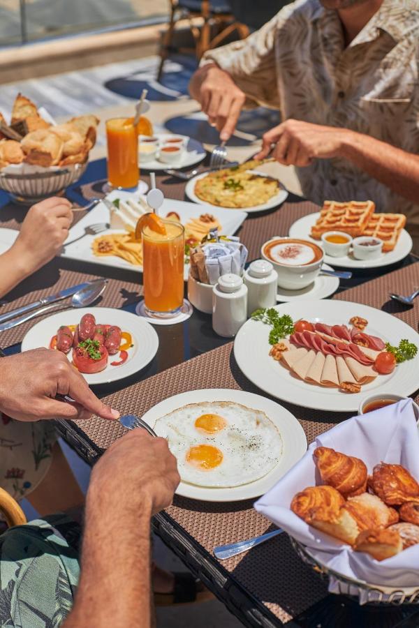 Tolip Resort El Galala Majestic Ain Suchna Exterior foto The photo features a spread of breakfast dishes on a table. There are two sunny-side-up eggs on one plate, surrounded by various food items, including slices of ham, sausages, and fresh tomatoes. Another plate holds a serving of waffles. A bowl with 