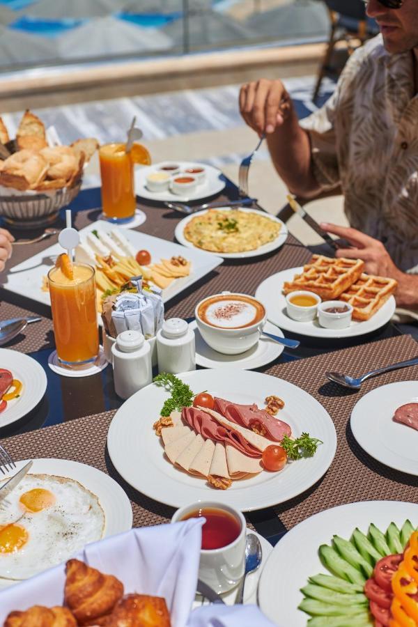 Tolip Resort El Galala Majestic Ain Suchna Exterior foto The photo shows a breakfast spread laid out on a table. There are several plates with a variety of food items, including:

1. **Sliced Cold Cuts**: A plate featuring various cold meats, accompanied by garnishes like cherry tomatoes and lettuce.
2. **