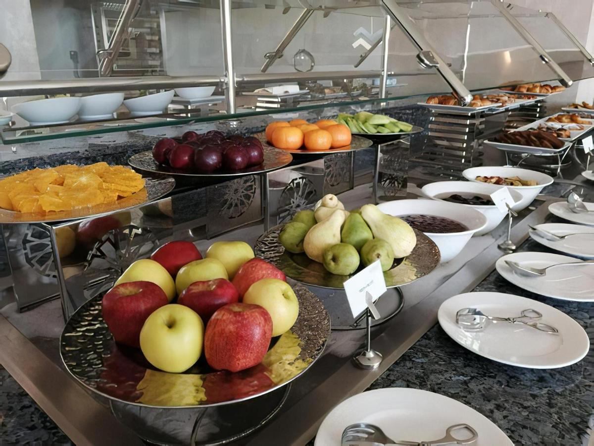 Tolip Resort El Galala Majestic Ain Suchna Exterior foto The photo displays a buffet setup featuring an assortment of fresh fruits arranged on several tiered trays. There are red and green apples, pears, grapes, and oranges. Adjacent to the fruit display, there are several bowls containing various other fo