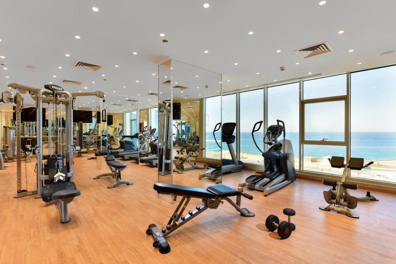 Tolip Resort El Galala Majestic Ain Suchna Exterior foto The photo shows a modern gym interior with a variety of fitness equipment. There are cardio machines like treadmills and ellipticals, along with strength training equipment such as free weights and benches. The gym features large windows that offer a