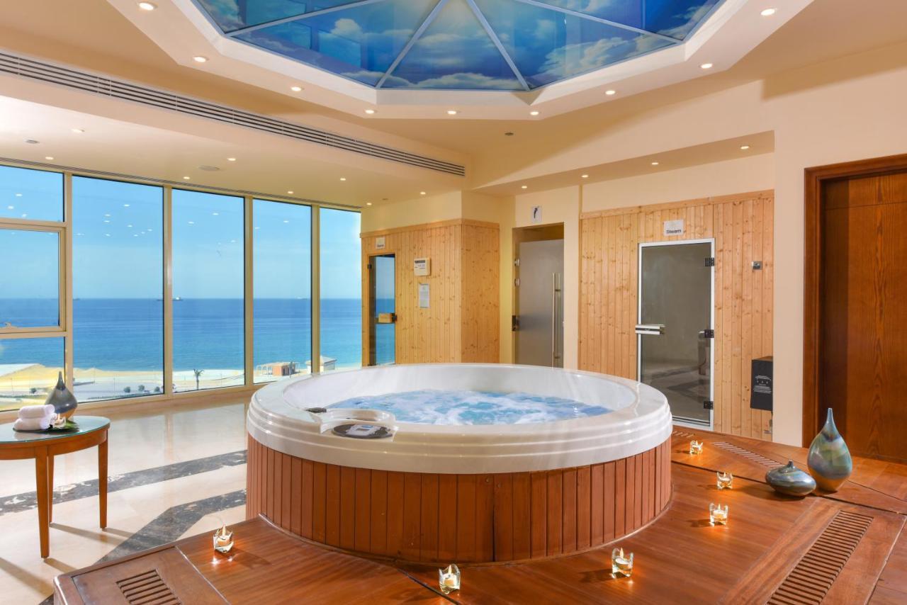 Tolip Resort El Galala Majestic Ain Suchna Exterior foto The photo shows a luxurious spa room featuring a large, round hot tub positioned in the center. The walls are mostly glass, offering a stunning view of the ocean. The ceiling has a painted sky, enhancing the serene atmosphere. There are wooden elemen