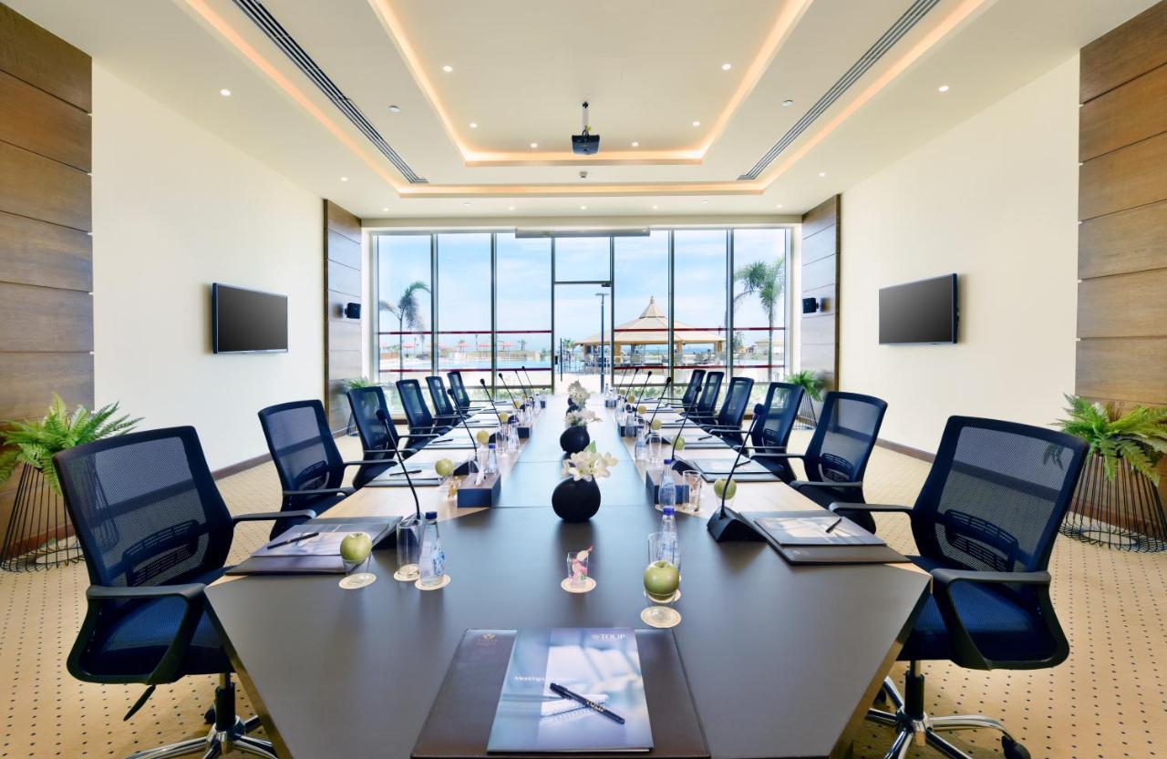 Tolip Resort El Galala Majestic Ain Suchna Exterior foto The image shows a modern conference room with a large, dark rectangular table surrounded by ergonomic black chairs. The room features large windows that allow natural light to enter and provide a view of the outdoors, including some greenery. On the 