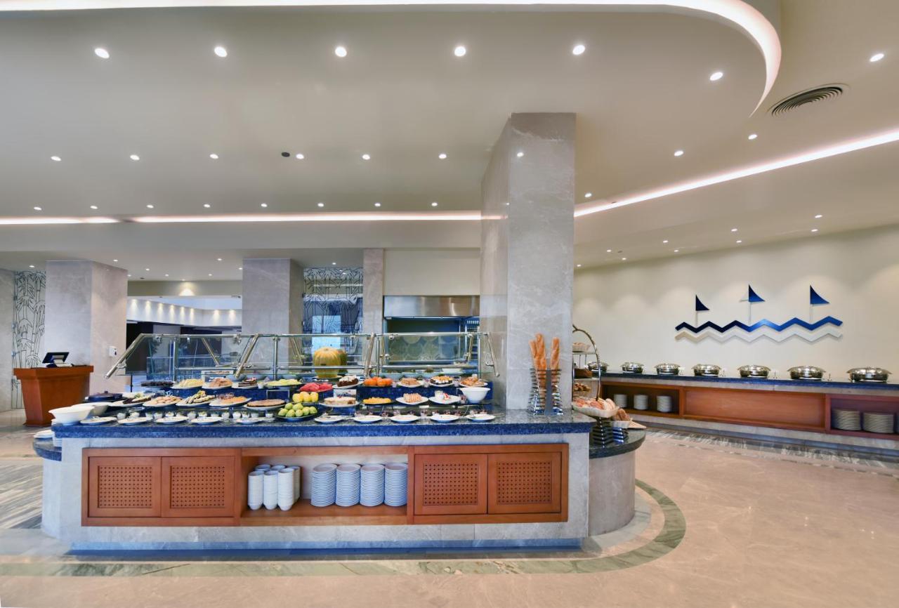 Tolip Resort El Galala Majestic Ain Suchna Exterior foto The image shows a buffet-style dining area in a restaurant or hotel. There are several food stations with a variety of dishes displayed, including fruits, salads, and other food items. The layout features a large, central island with a wooden base an