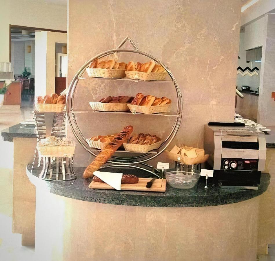 Tolip Resort El Galala Majestic Ain Suchna Exterior foto The photo shows a display of various types of bread and pastries arranged on a countertop. There are several baskets stacked on a circular stand, filled with different baked goods like croissants and rolls. A long baguette is placed horizontally on a