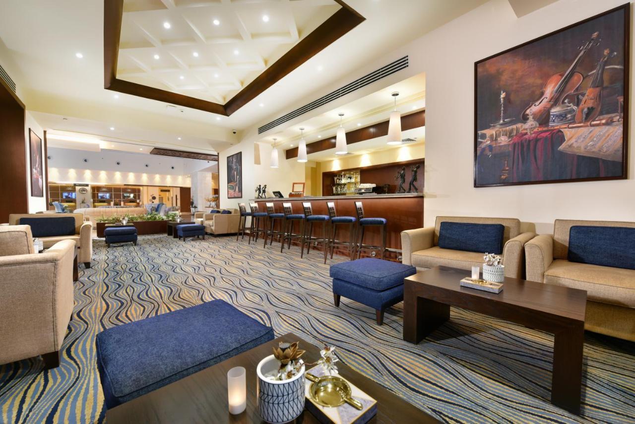 Tolip Resort El Galala Majestic Ain Suchna Exterior foto The photo depicts a modern, inviting lobby or lounge area. It features a cozy seating arrangement with light-colored sofas and deep blue accent chairs. In the center, there is a low wooden coffee table with decorative items, including a candle and sm