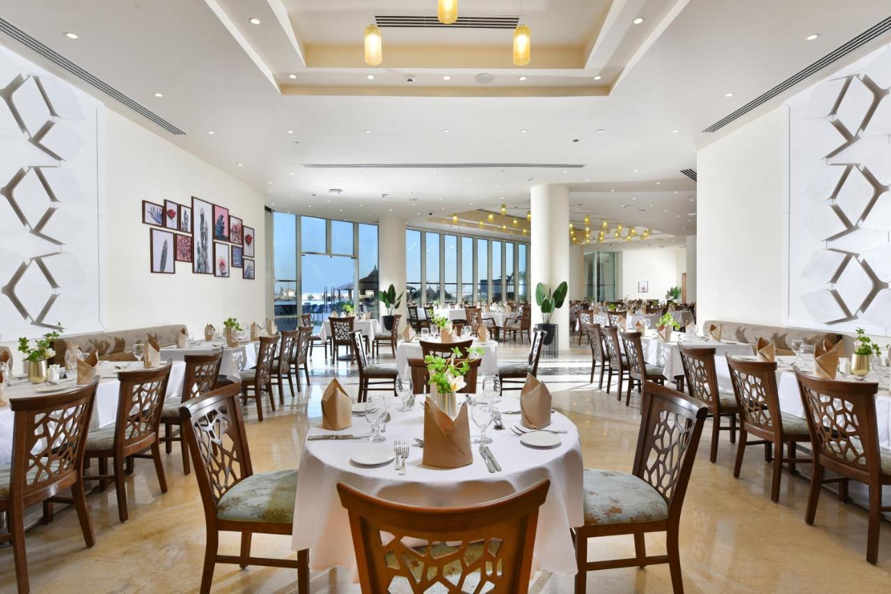 Tolip Resort El Galala Majestic Ain Suchna Exterior foto The photo displays a spacious and elegantly designed restaurant interior. It features numerous tables set for dining, with white tablecloths, neatly folded napkins, and decorative centerpieces of flowers. The seating consists of wooden chairs that co