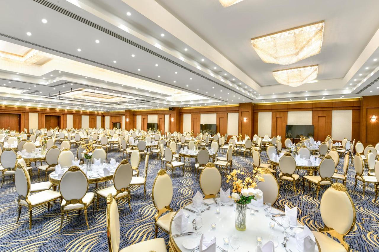 Tolip Resort El Galala Majestic Ain Suchna Exterior foto The photo shows a spacious and elegantly decorated banquet hall. The room features numerous round dining tables, each set with white tablecloths and adorned with decorative centerpieces, likely flowers. The chairs surrounding the tables have a luxuri